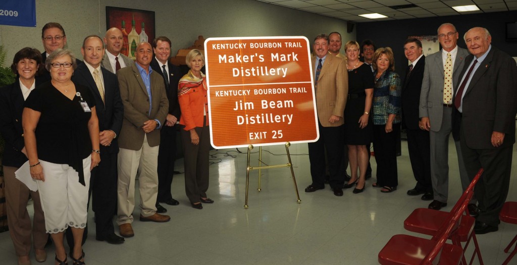 Representatives from the Kentucky Bourbon industry join First Lady Jane Beshear and elected officials in unveiling the first of 17 new Kentucky Bourbon Trail interstate signs. (Left to right): Rep. Linda Belcher; Geri Grigsby (Kentucky Transportation Cabinet); Sen. Jimmy Higdon; Jeff Conder (Beam Global Spirits & Wine); Versailles Mayor Fred Siegelman; KDA President Eric Gregory; First Lady Jane Beshear; Kevin Smith (Maker’s Mark); Greg Davis (Maker’s Mark); Marnie Walters (Woodford Reserve); Larry Kass (Heaven Hill); Secretary Marcheta Sparrow (Tourism, Arts & Heritage Cabinet); Franklin County Judge-Executive Ted Collins; Jim Rutledge (Four Roses); Jimmy Russell (Wild Turkey).