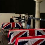 Judi Dench as in M in Skyfall stands behind the coffins of British Soldiers with flags draped in Union Jack Flags. This Bond is Judi Dench’s last role as M